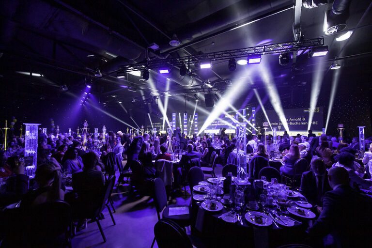 Image of an award show with purple lighting and tables of food