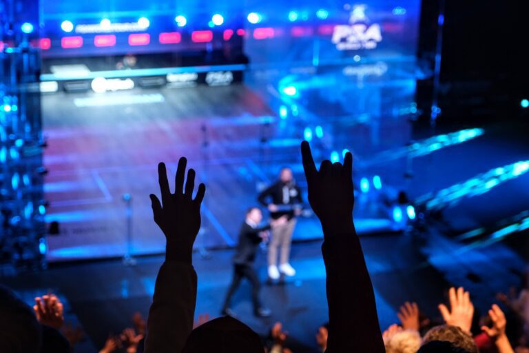Photo of hands up in the crowd whilst a man is playing the guitar