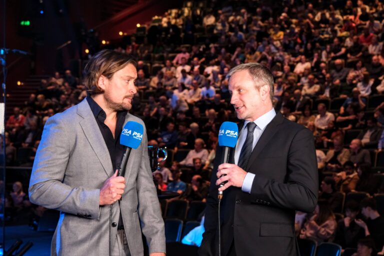 Image of two men talking at the PSA with a crowd behind them